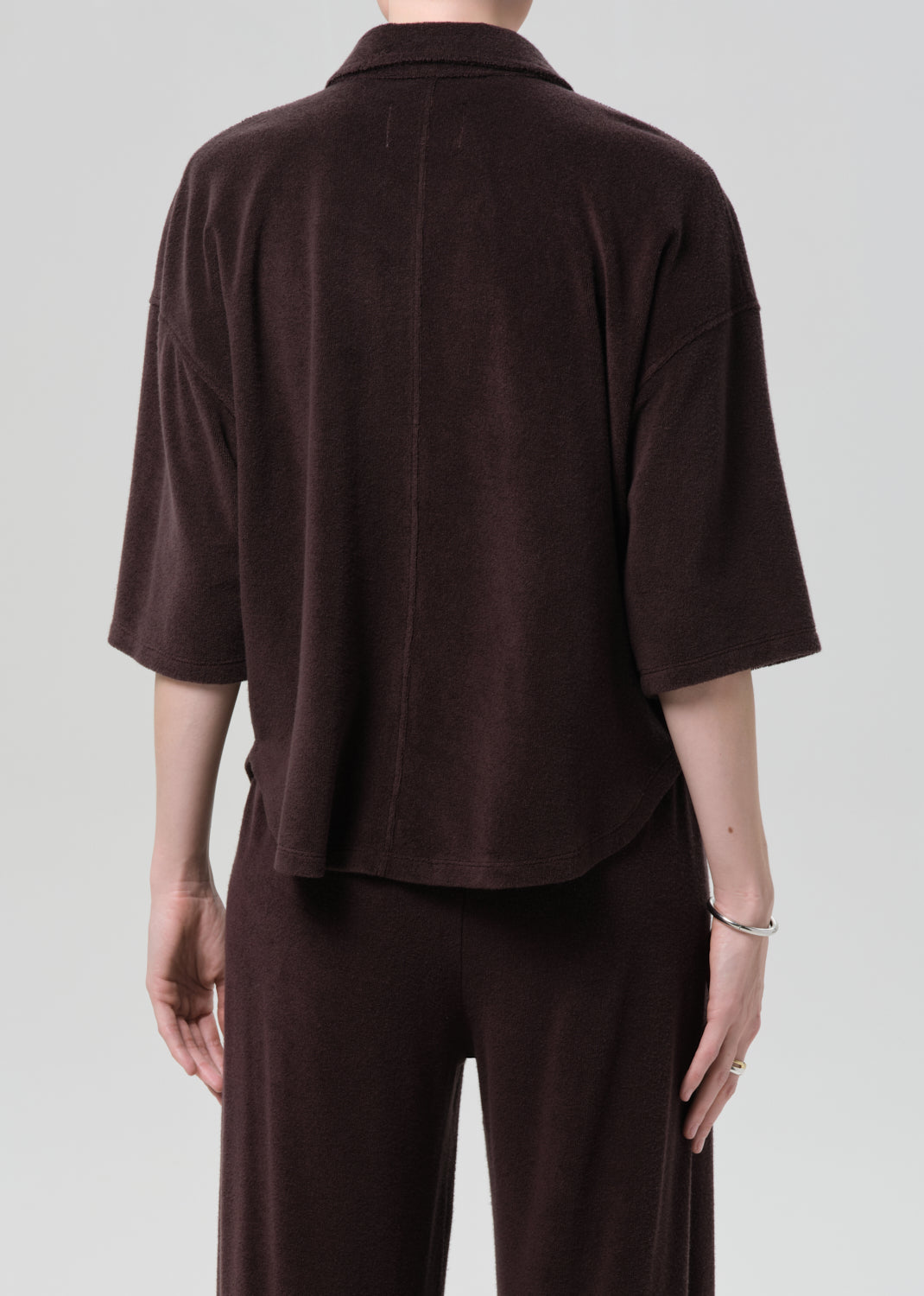 Person wearing a brown terry outfit with a deep neckline on a plain background