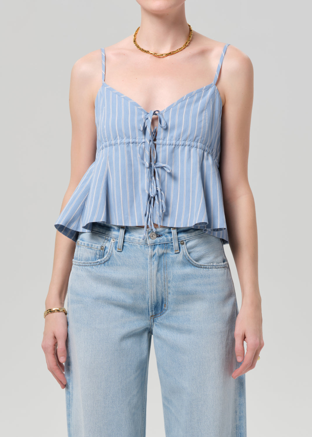 Woman wearing a blue striped top and light blue jeans against a gray background