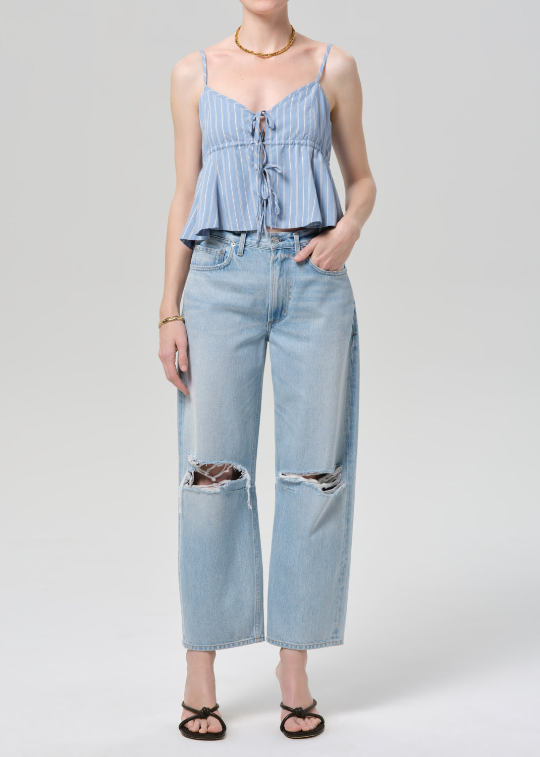 Person wearing a blue striped top and ripped jeans on a grey background