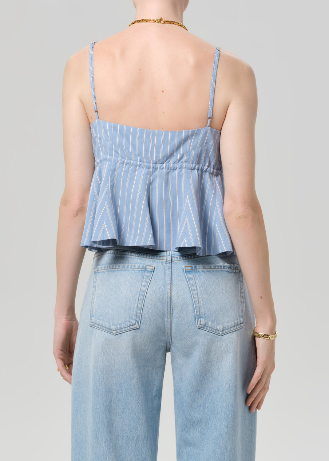 Person wearing a blue striped peplum top and light blue jeans on a gray background