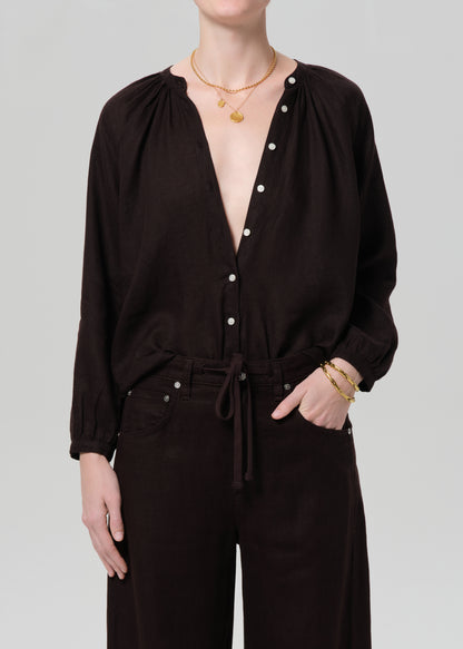 Person wearing a dark brown outfit with white buttons on a plain background