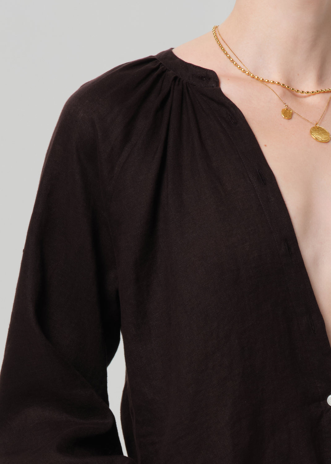 Brown blouse with a plunging neckline and gold necklaces on a gray background