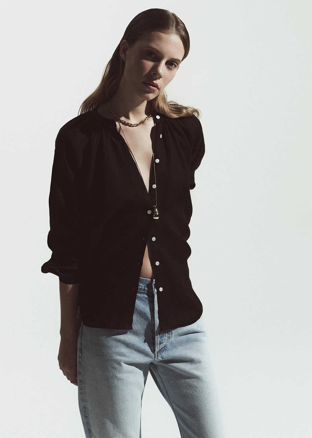 Woman wearing a brown button-up shirt and light blue jeans against a white background