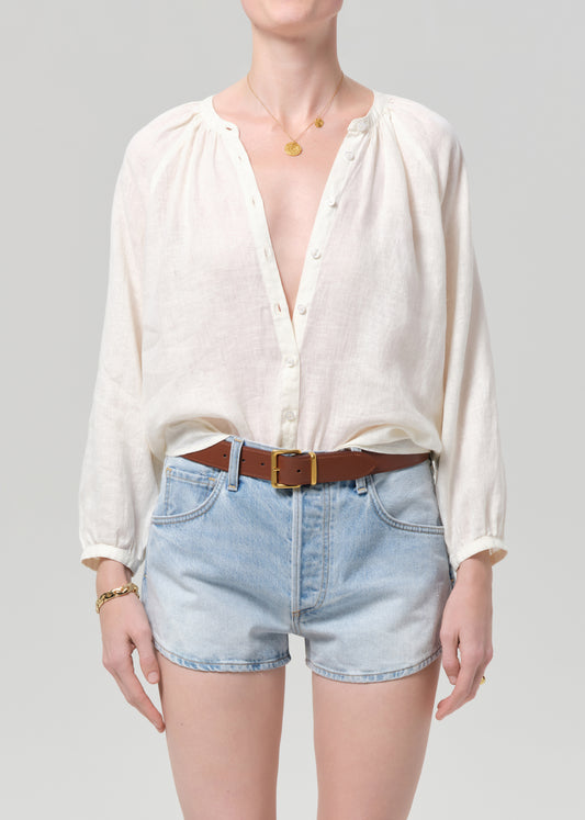 Person wearing a white blouse and denim shorts on a gray background