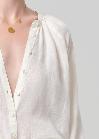 White button-up shirt with a gold necklace on a plain background
