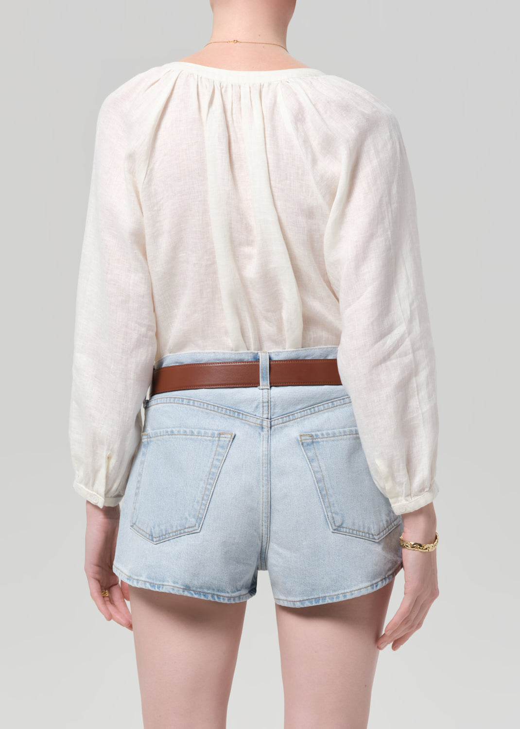 Person wearing a cream blouse and denim shorts on a plain background