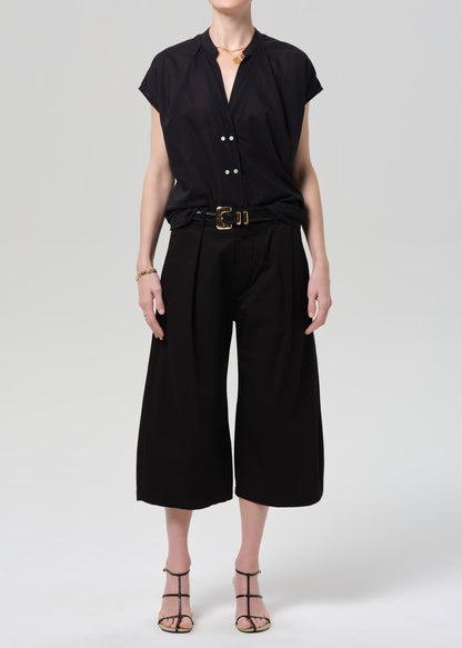 Person wearing a black blouse and black pants with a gold belt on a gray background