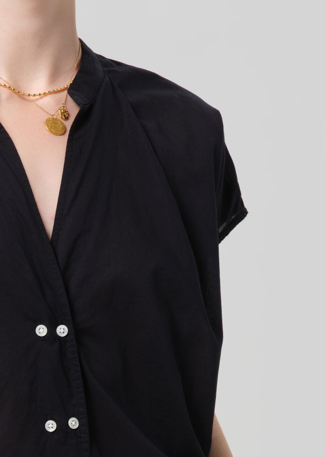 Person wearing a black blouse and black pants with a gold belt on a gray background