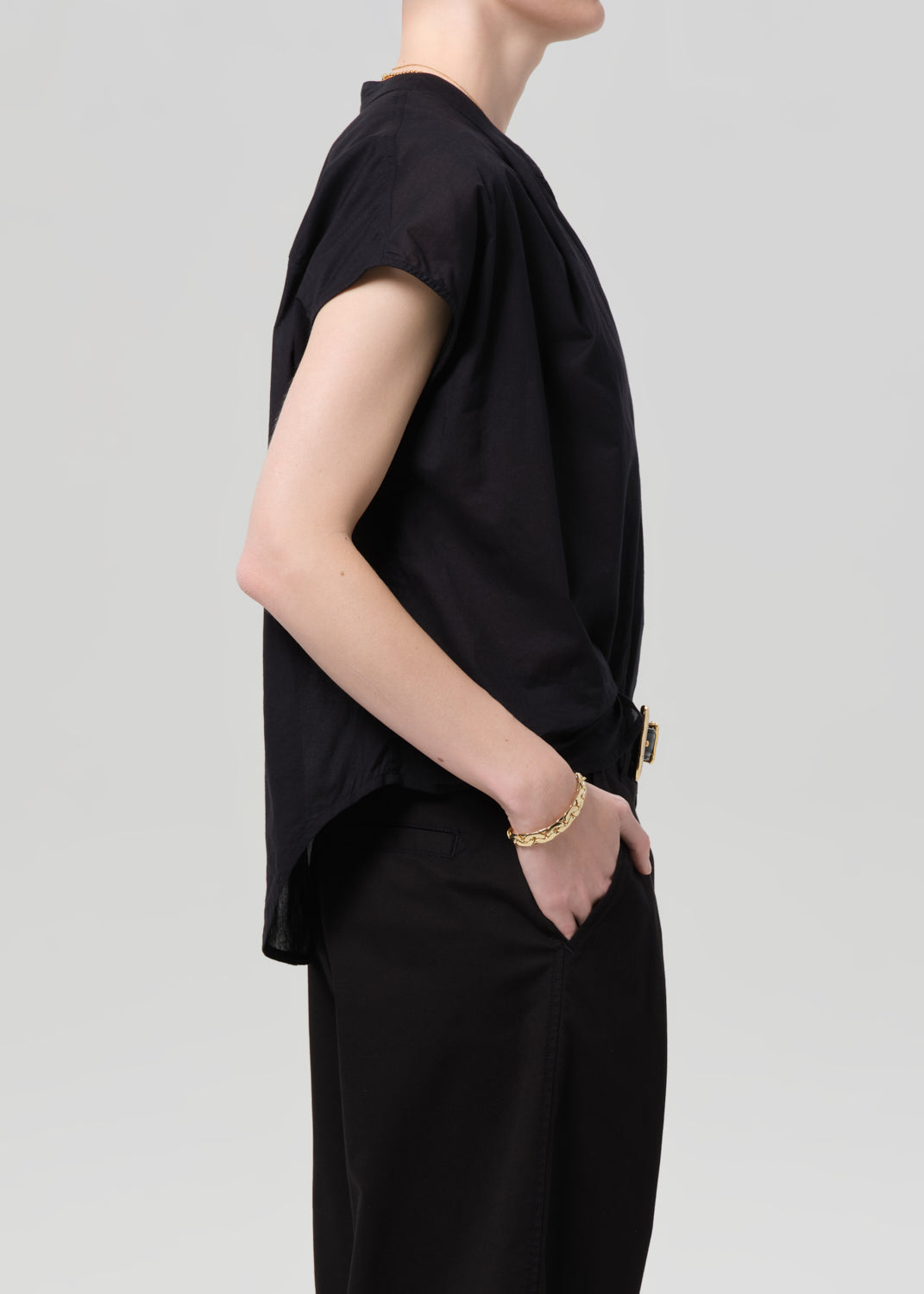 Person wearing a black blouse and black pants with a gold belt on a gray background