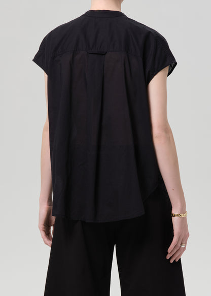 Person wearing a black blouse and black pants with a gold belt on a gray background
