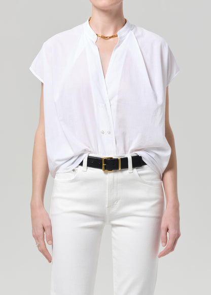 Person wearing a white blouse and white pants with a black belt on a plain background