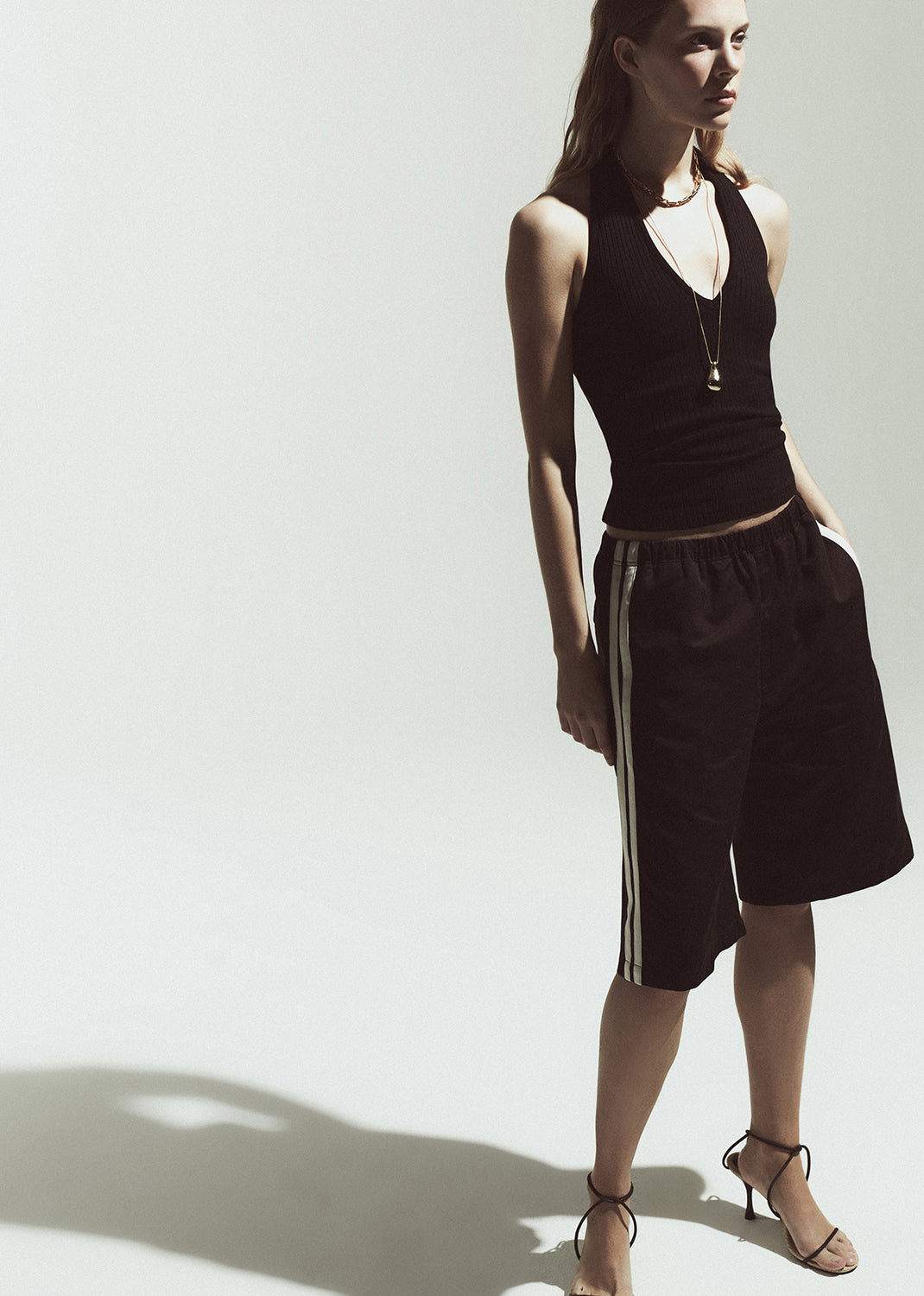 Woman wearing a black halter top and brown shorts with stripes on a white background