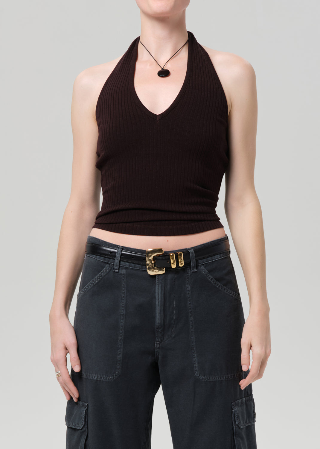 Person wearing a brown halter top and black cargo pants on a gray background