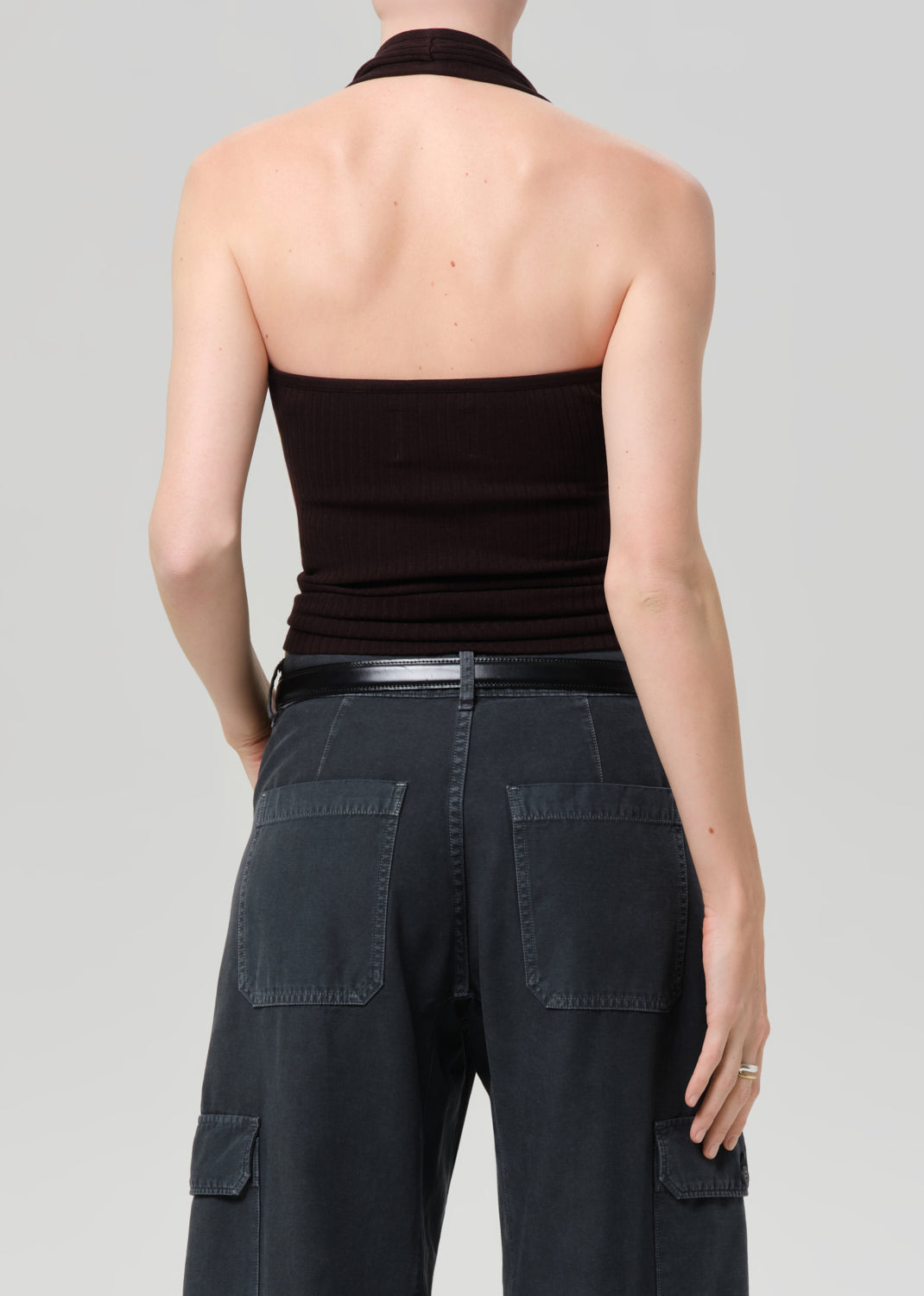 Person wearing a brown halter top and dark cargo pants on a plain background