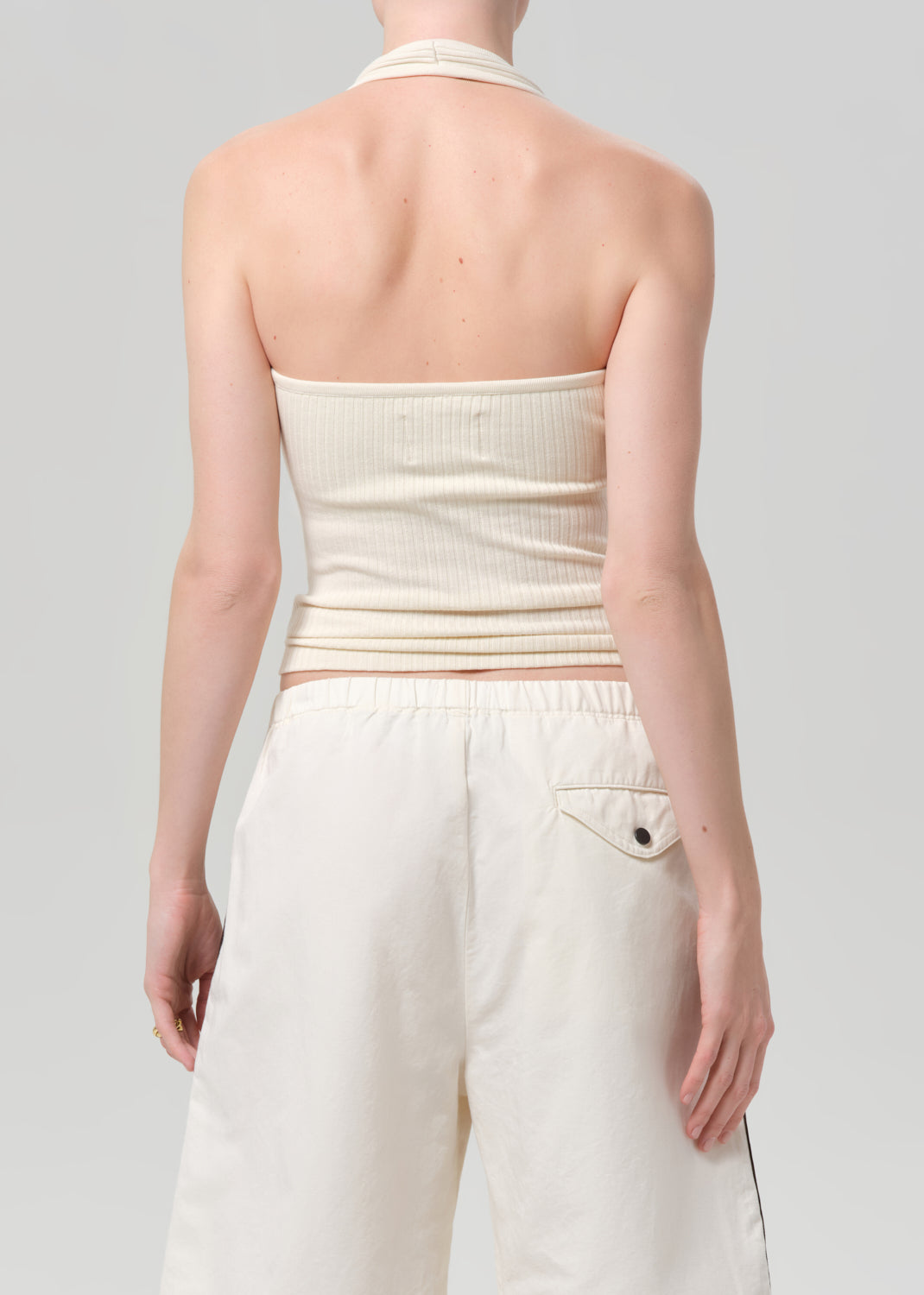 Person wearing a cream halter top and white shorts on a light gray background