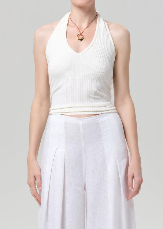 Person wearing a white halter top and flowing white pants on a light gray background