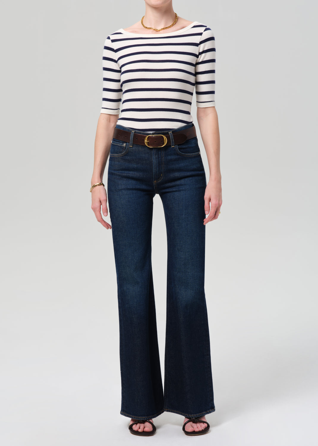 Person wearing a striped shirt and blue jeans on a grey background