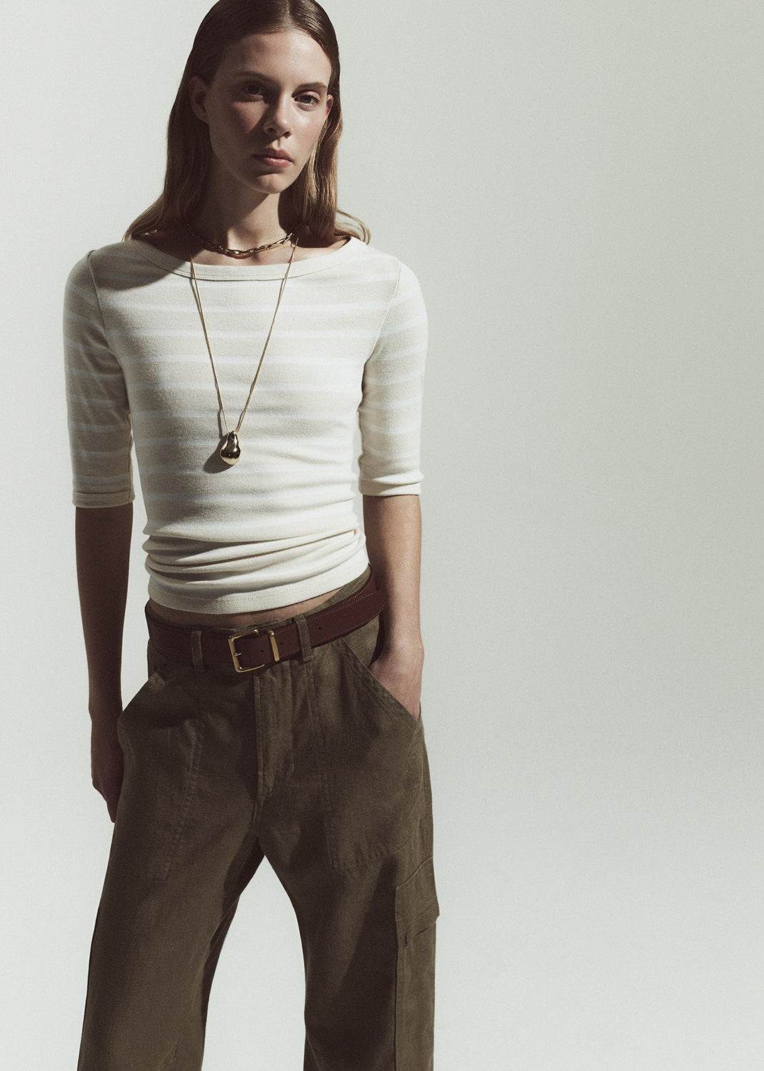 Person wearing a striped top and brown pants with a necklace on a plain background