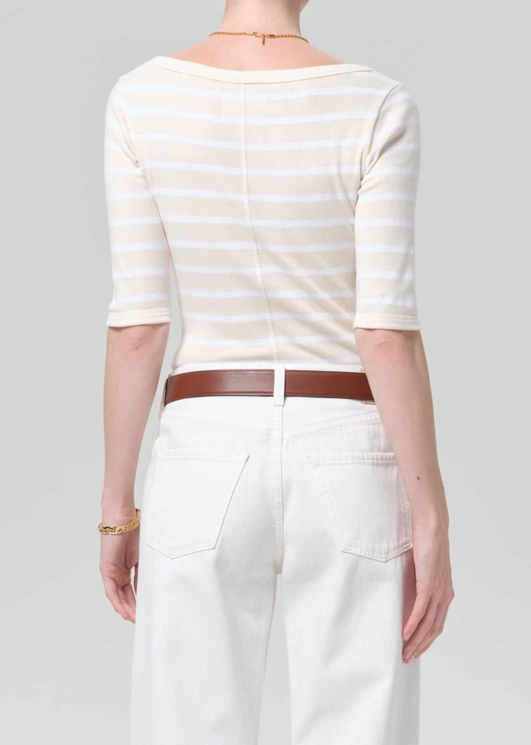 Person wearing a striped shirt and white pants with a brown belt on a gray background