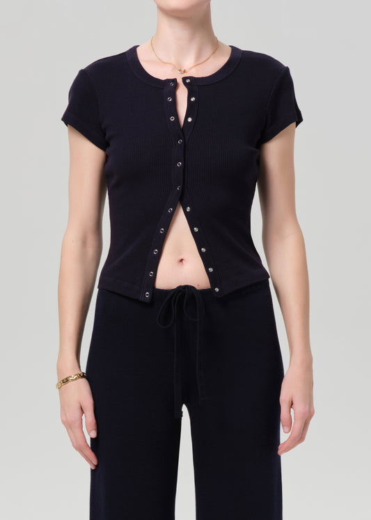 Person wearing a navy short-sleeve top with button details and navy pants on a light gray background