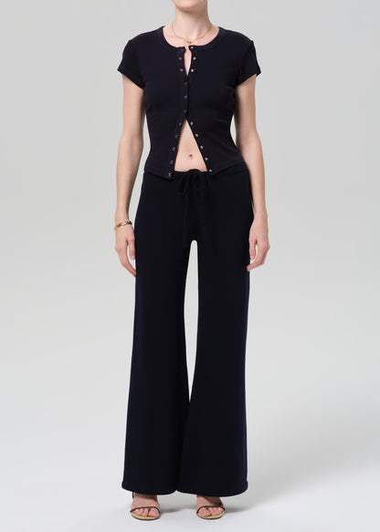 Person wearing a navy short-sleeve top with button details and navy pants on a light gray background