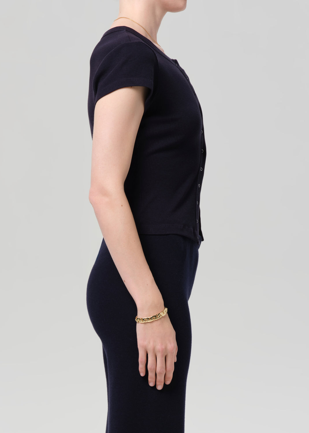 Person wearing a navy short-sleeve top with button details and navy pants on a light gray background