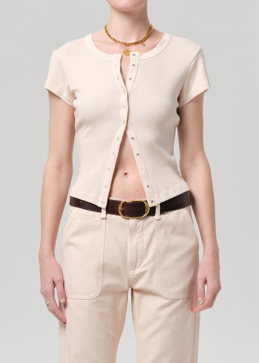 Person wearing a light peach short-sleeve button-up top and pants with a belt on a gray background