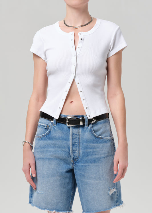 Person wearing a white button-up shirt and blue denim shorts on a gray background