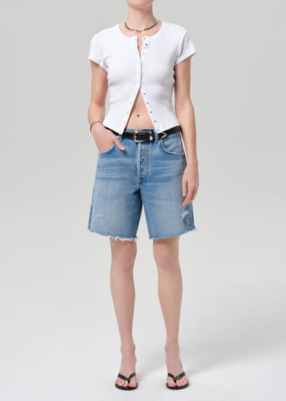 Person wearing a white short-sleeve shirt and denim shorts on a plain background