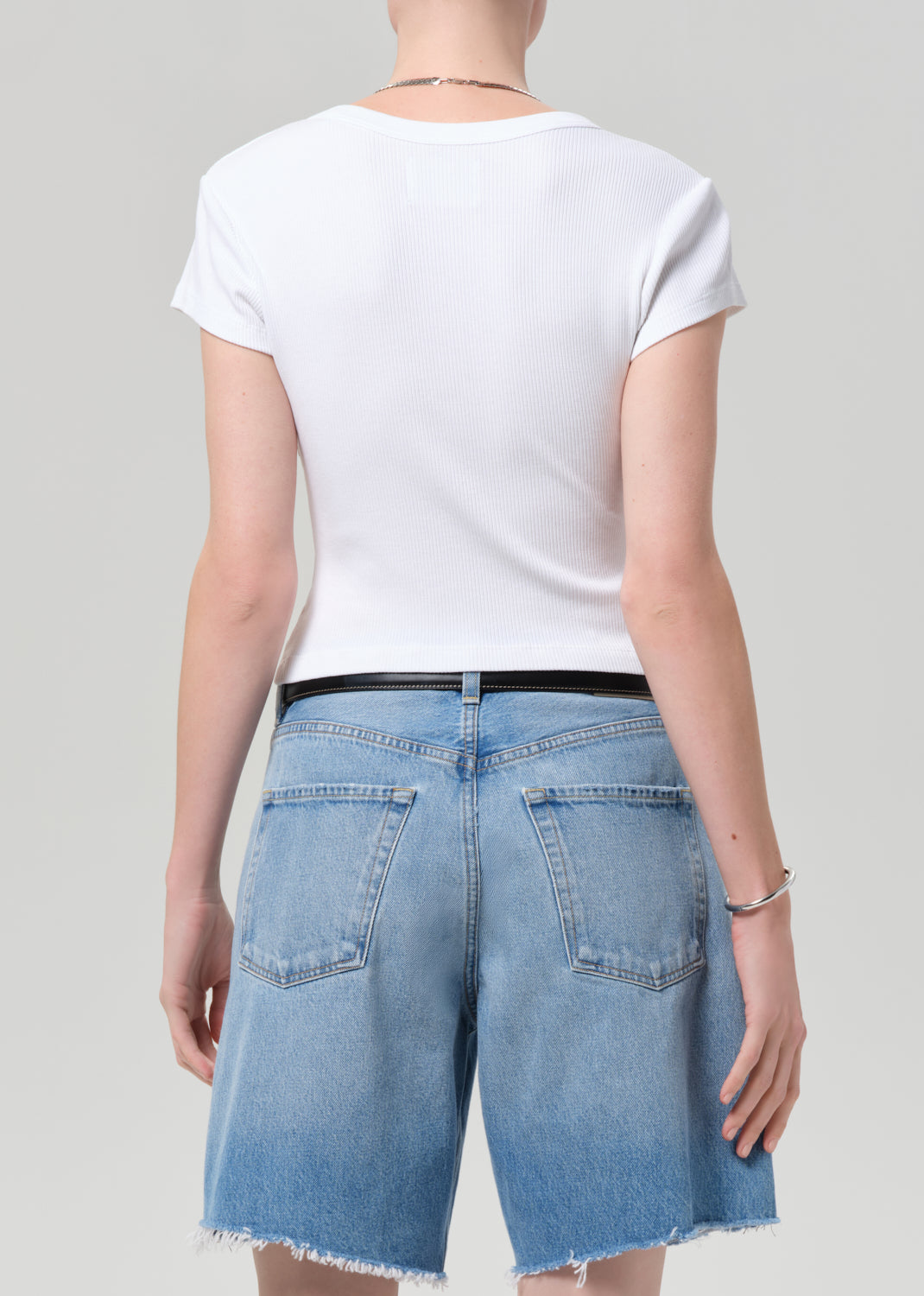 Person wearing a white t-shirt and denim shorts on a plain background