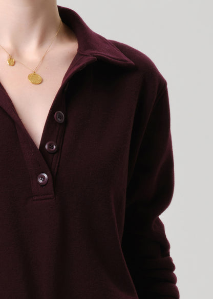 Close-up of a person wearing a dark brown long-sleeve shirt with buttons on a grey background