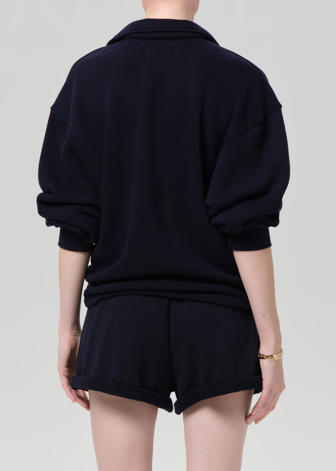 Person wearing a navy outfit with a matching sweatshirt and shorts on a gray background