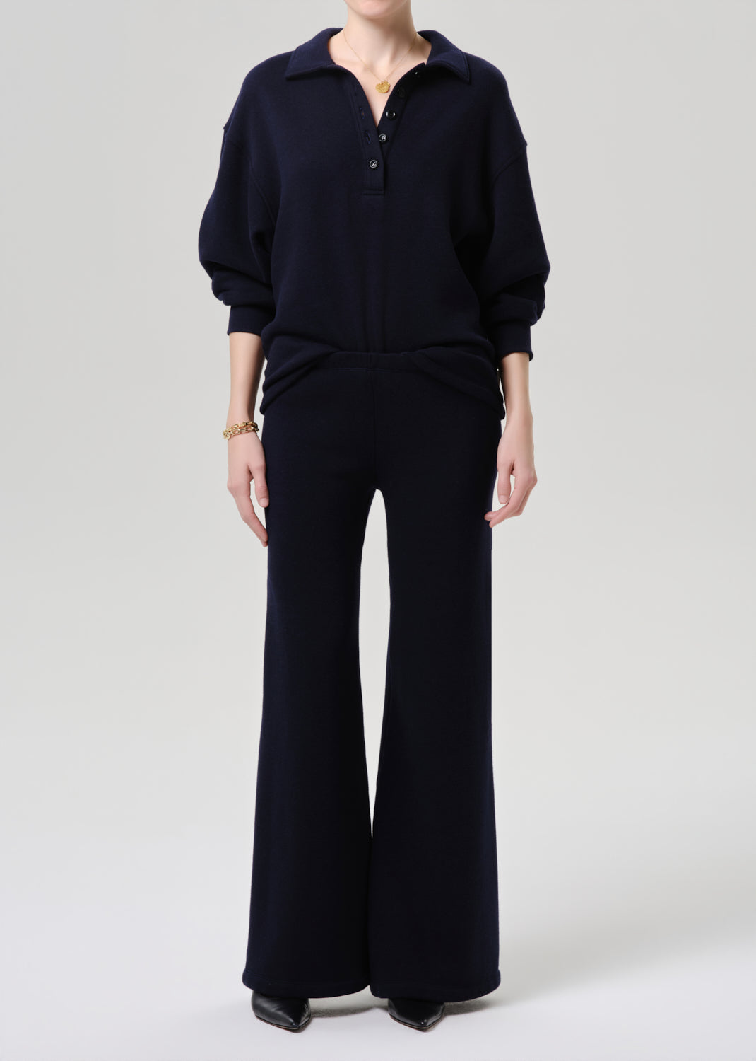 A model wearing a dark navy blue knit two-piece set consisting of a long-sleeve polo-style top and matching wide-leg trousers, photographed against a grey background.