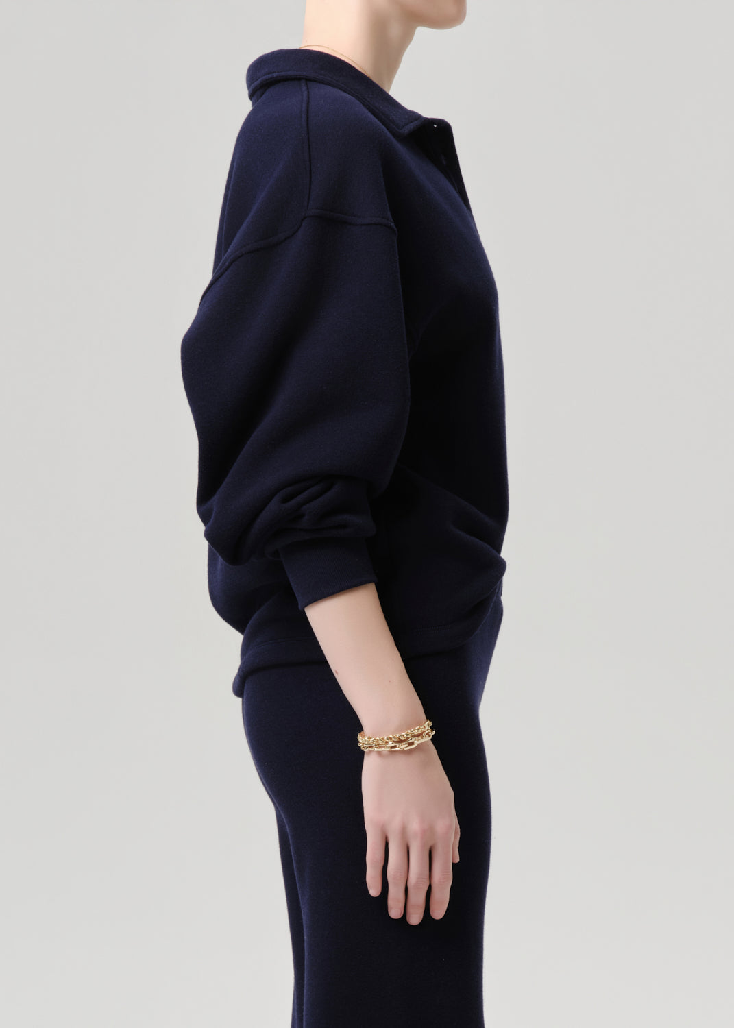 Person wearing a navy blue outfit with a gold bracelet on a grey background