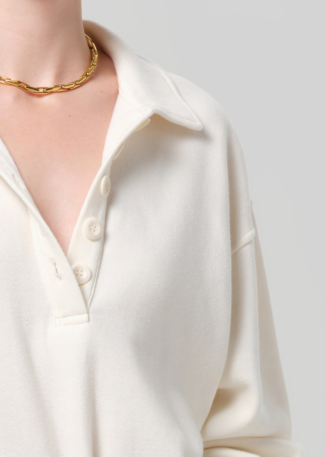 Close-up of a person wearing a sweatshirt  with a gold necklace on a light gray background