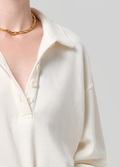 Close-up of a person wearing a sweatshirt  with a gold necklace on a light gray background