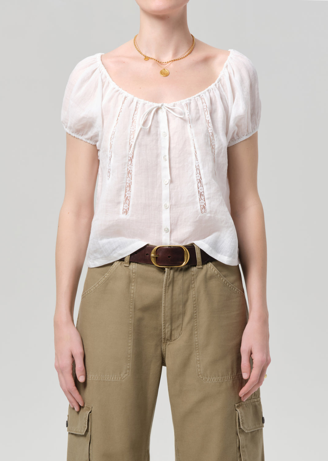 Person wearing a white blouse and beige pants on a gray background