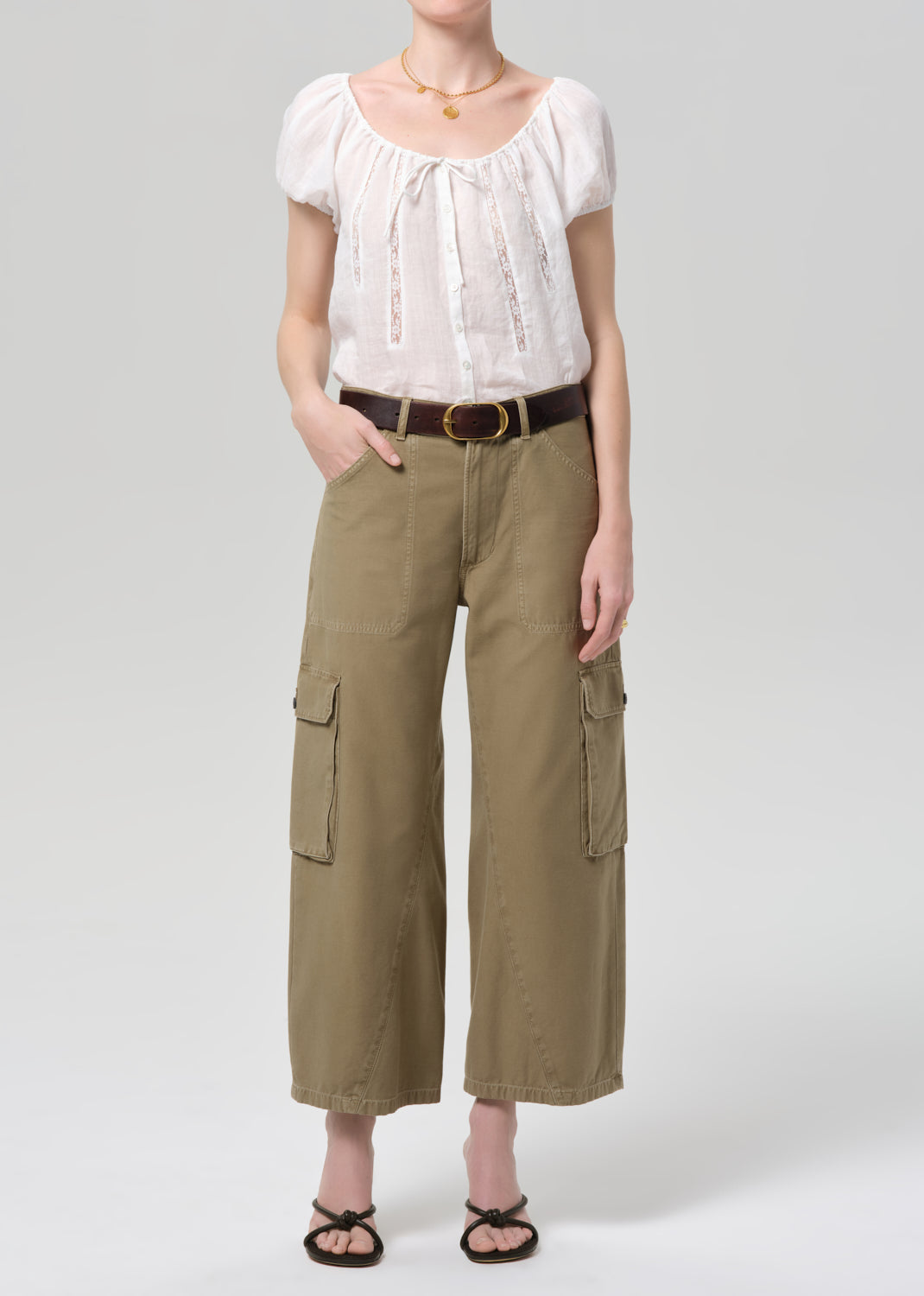 Person wearing a white blouse and khaki cargo pants on a plain background