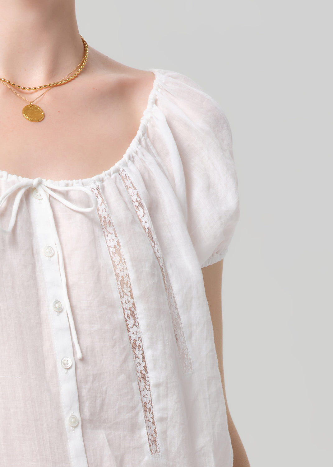 White blouse with lace trim and gold necklace on a plain background