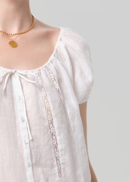 White blouse with lace trim and gold necklace on a plain background