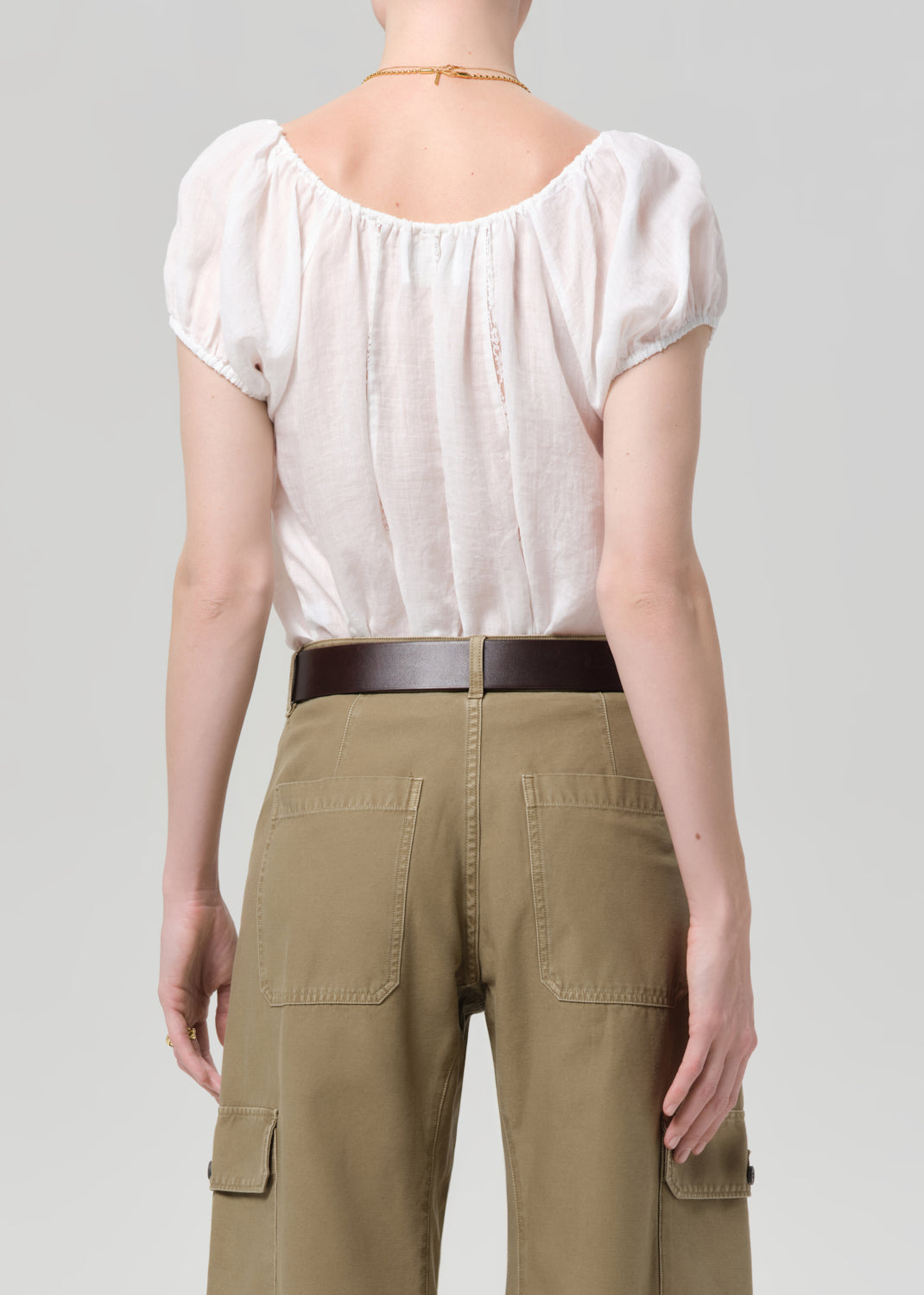Person wearing a white blouse and green cargo pants on a plain background