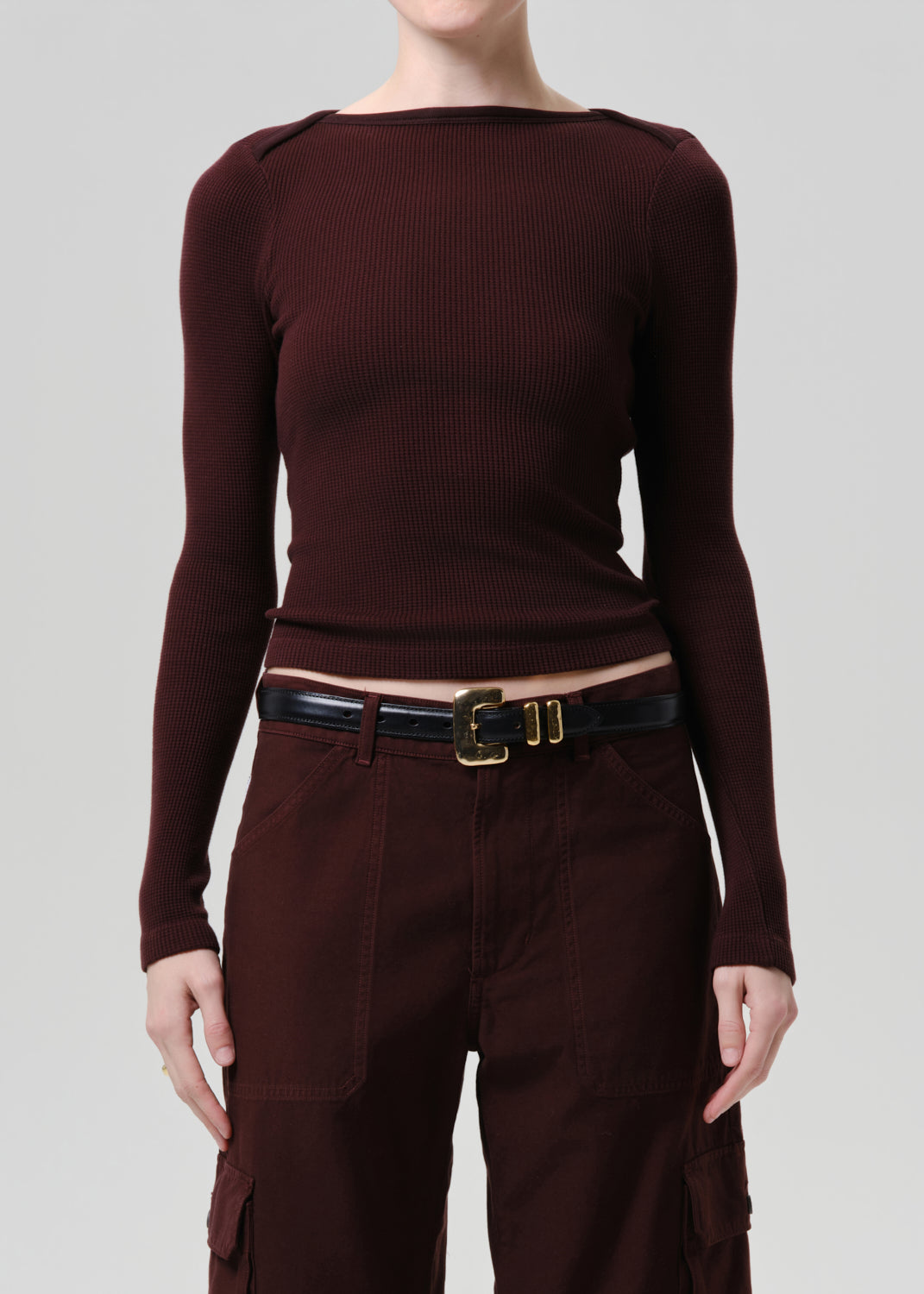 Person wearing a purple brown long-sleeve top and pants with a belt on a grey background