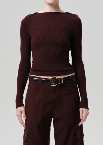 Person wearing a purple brown long-sleeve top and pants with a belt on a grey background