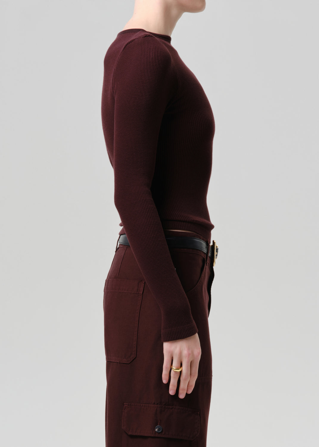 Person wearing a purple brown long-sleeve top and pants on a grey background