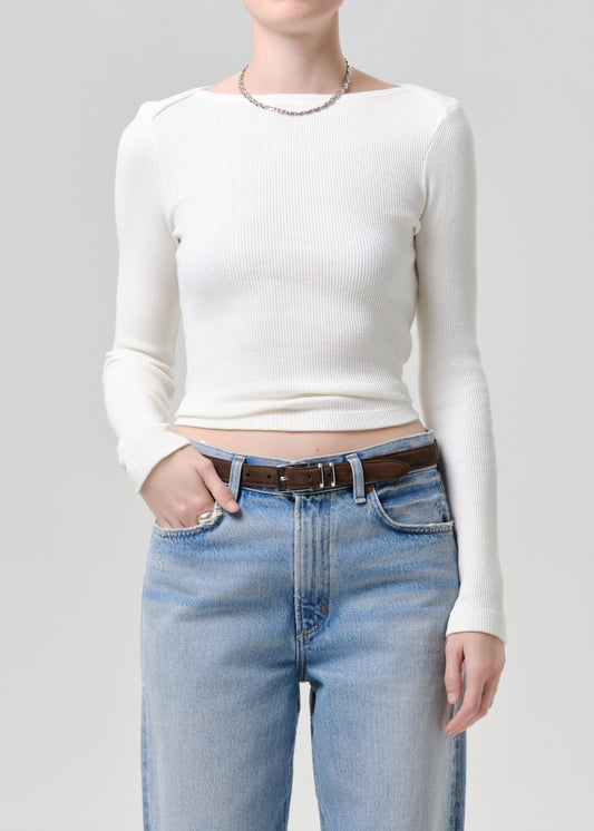 Person wearing a white long-sleeve top and blue jeans on a grey background