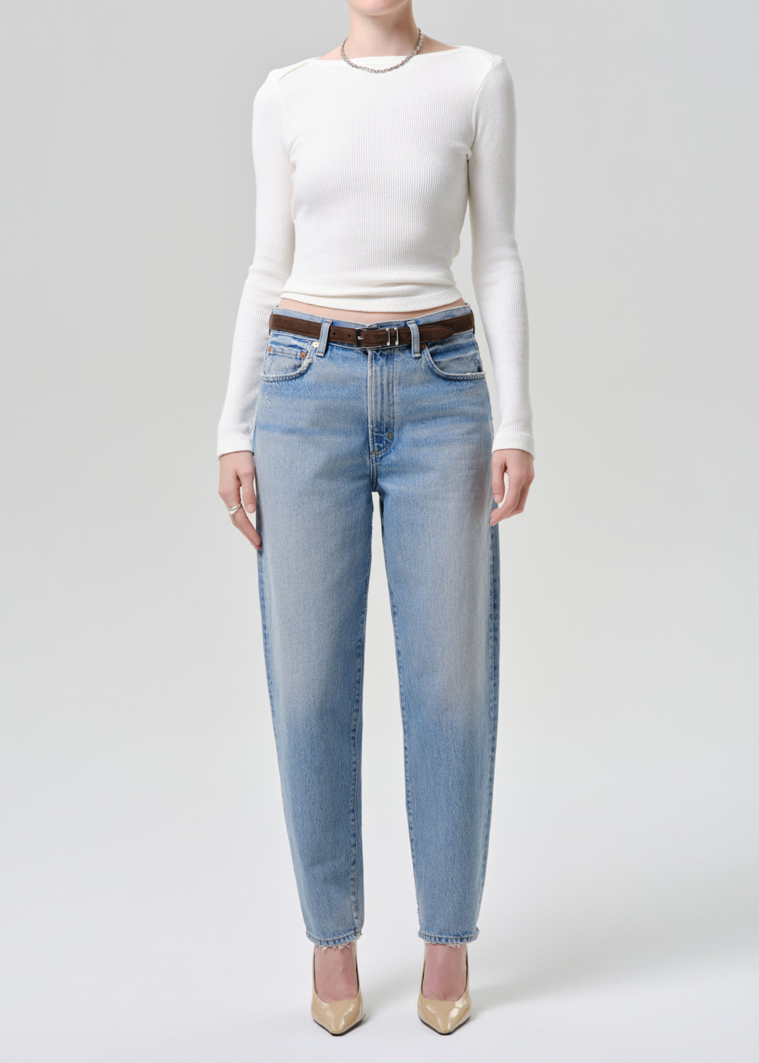 Person wearing a white long-sleeve top and light blue jeans on a grey  background