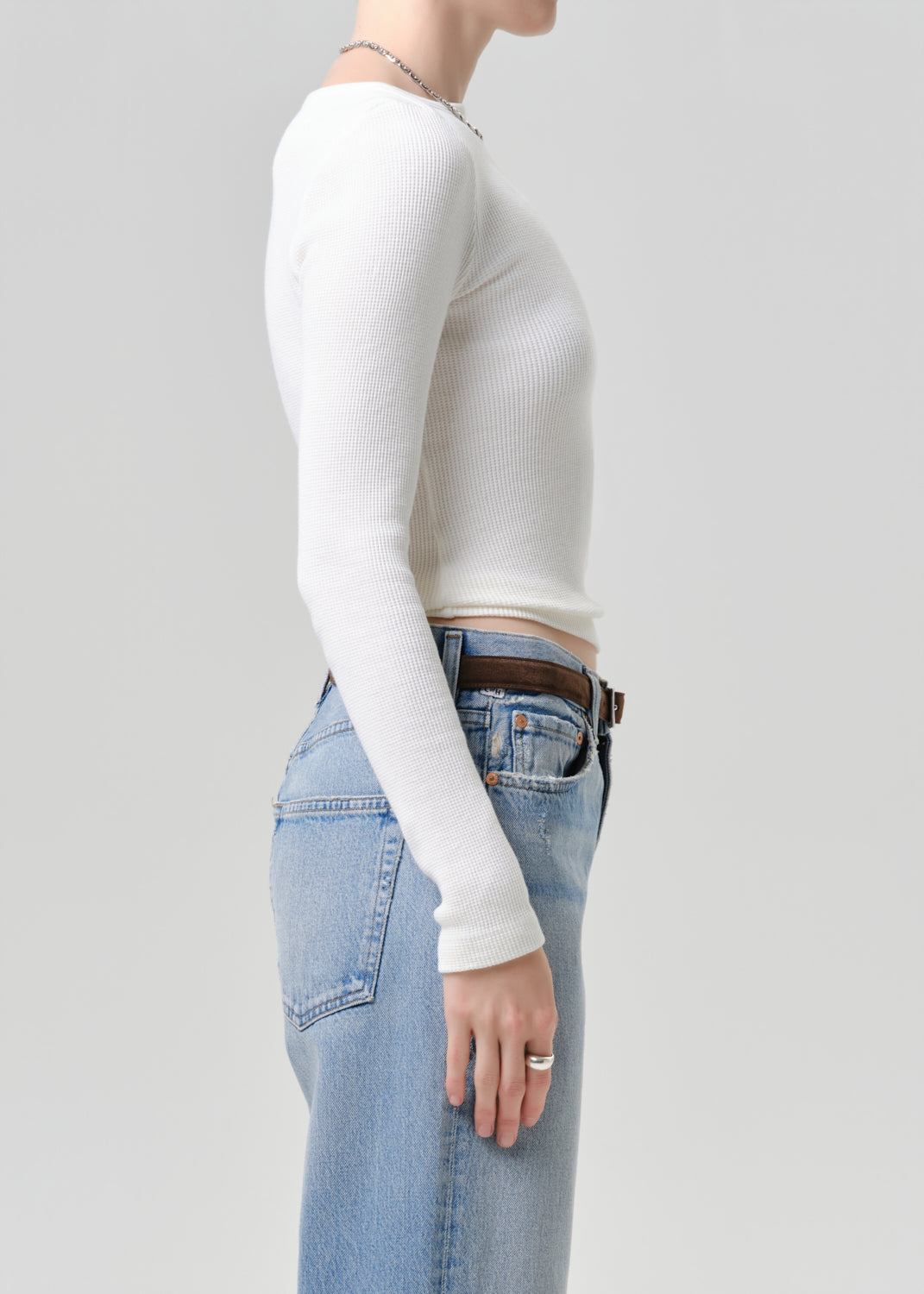 Person wearing a white long-sleeve top and blue jeans on a grey  background