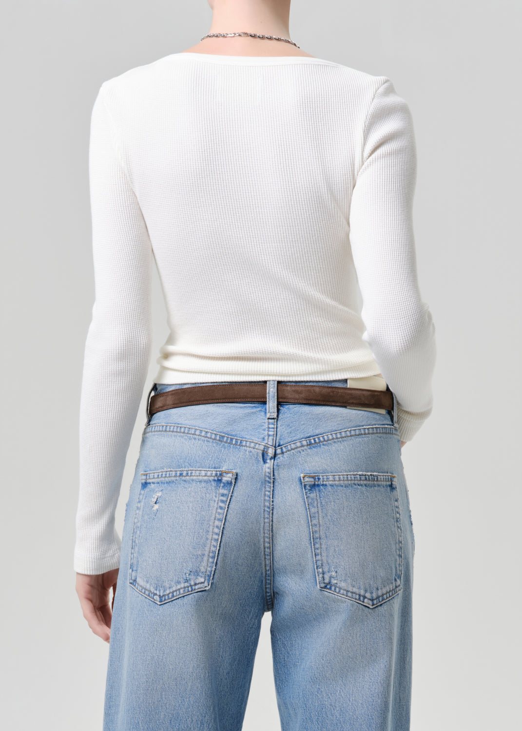 Person wearing a white long-sleeve top and light blue jeans on a grey background