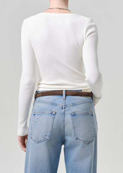 Person wearing a white long-sleeve top and light blue jeans on a grey background