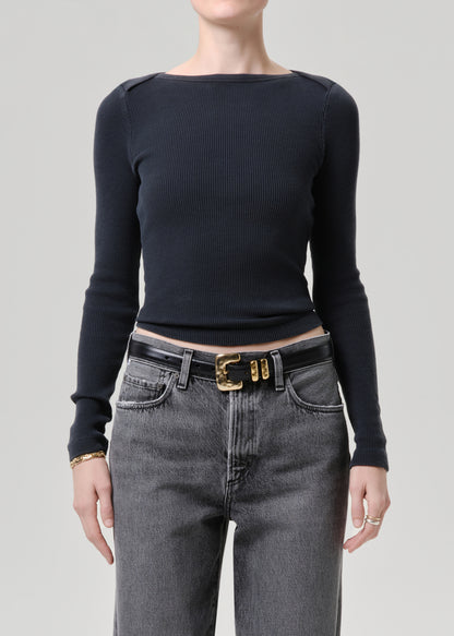 Person wearing a black long-sleeve top and gray jeans with a gold belt on a grey background